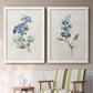 Set of two white barnwood framed canvas prints depicting two farmhouse botanical illustrations featuring blue periwinkle flowers with leafy stems above a sideboard in a cozy sitting room.