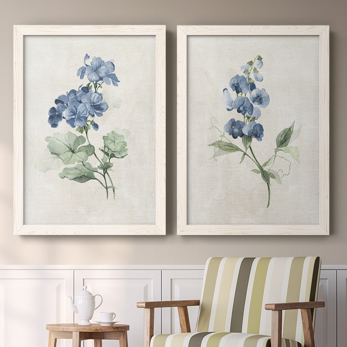 Set of two white barnwood framed canvas prints depicting two farmhouse botanical illustrations featuring blue periwinkle flowers with leafy stems above a sideboard in a cozy sitting room.
