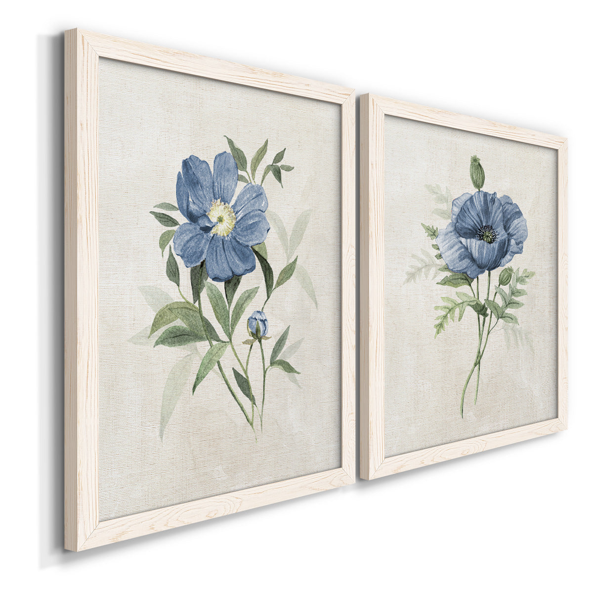 Angled view of a set of two white barnwood framed canvas prints featuring two farmhouse botanical illustrations featuring blue periwinkle flowers with leafy stems.