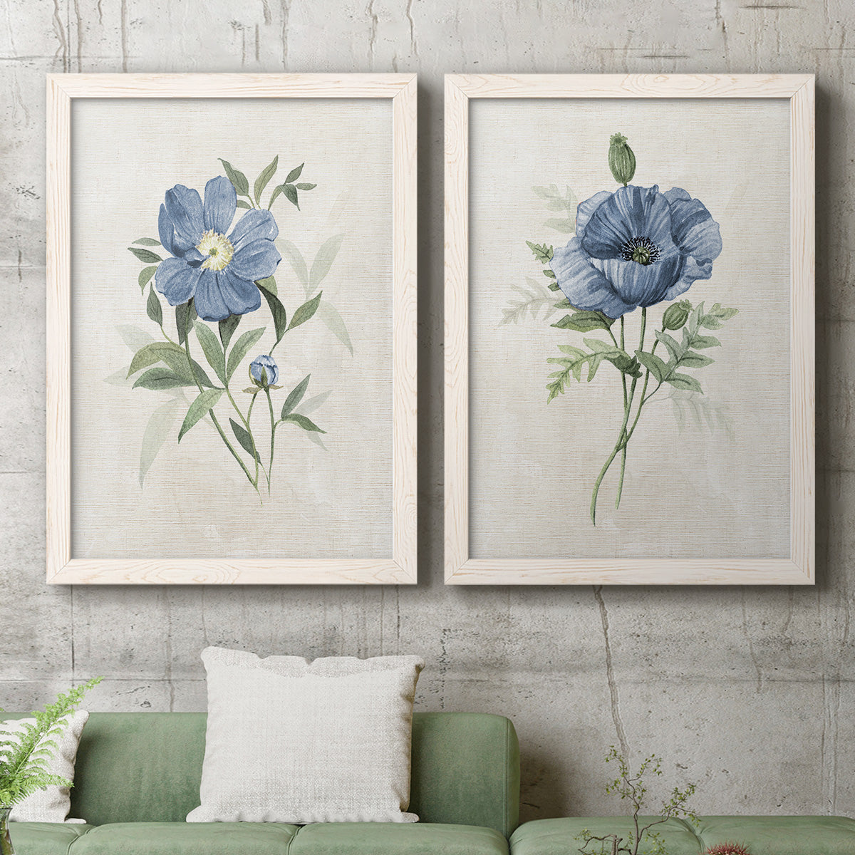 Set of two white barnwood framed canvas prints depicting a coordinated art pair of blue periwinkle flowers with leafy stems rendered as farmhouse botanical illustrations above a sofa in a modern living room.
