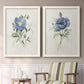 Set of two white barnwood framed canvas prints depicting two farmhouse botanical illustrations featuring blue periwinkle flowers with leafy stems above a sideboard in a cozy sitting room.