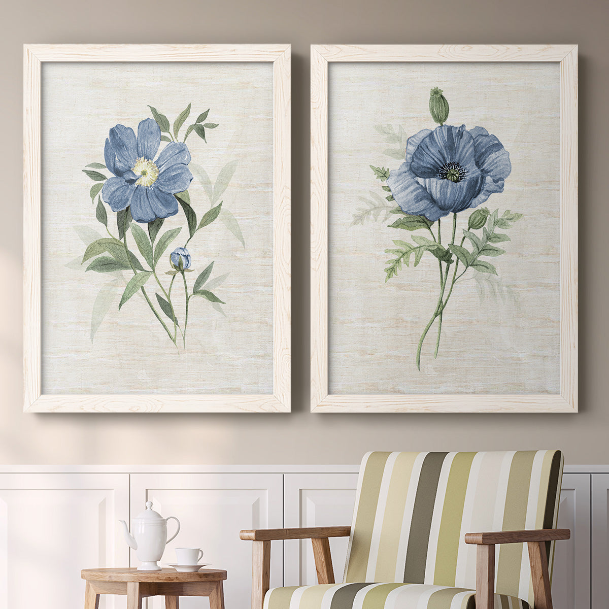 Set of two white barnwood framed canvas prints depicting two farmhouse botanical illustrations featuring blue periwinkle flowers with leafy stems above a sideboard in a cozy sitting room.