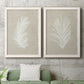 Set of two white barnwood framed canvas prints depicting a coordinated art pair of white palm frond silhouettes rendered as minimalist tropical botanical prints above a sofa in a modern living room.