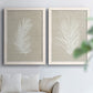 Set of two white barnwood framed canvas prints depicting feathery leaves, warm taupe grounds, and simple high-contrast shapes arranged across two complementary compositions above a sofa in a bright living space.