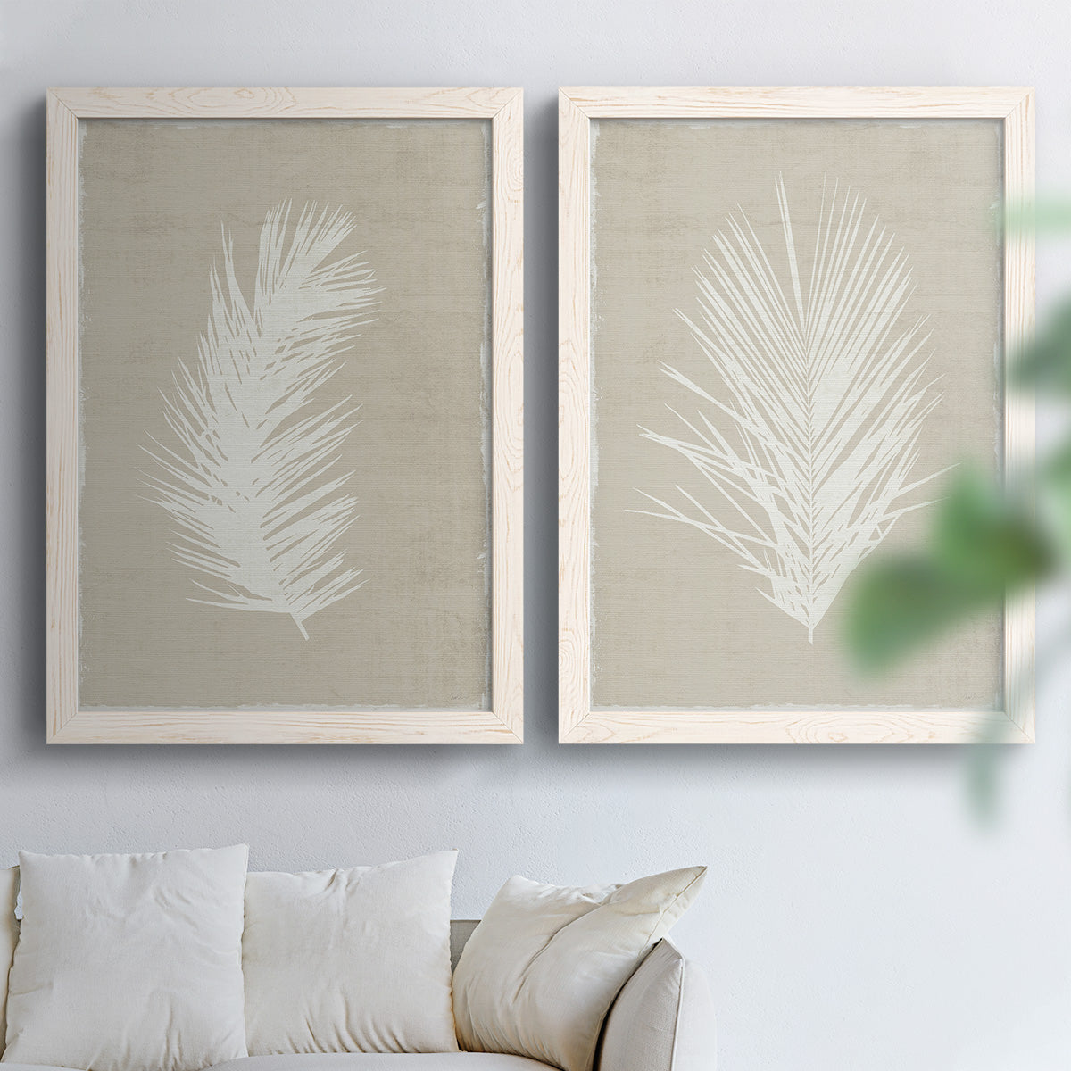 Set of two white barnwood framed canvas prints depicting feathery leaves, warm taupe grounds, and simple high-contrast shapes arranged across two complementary compositions above a sofa in a bright living space.