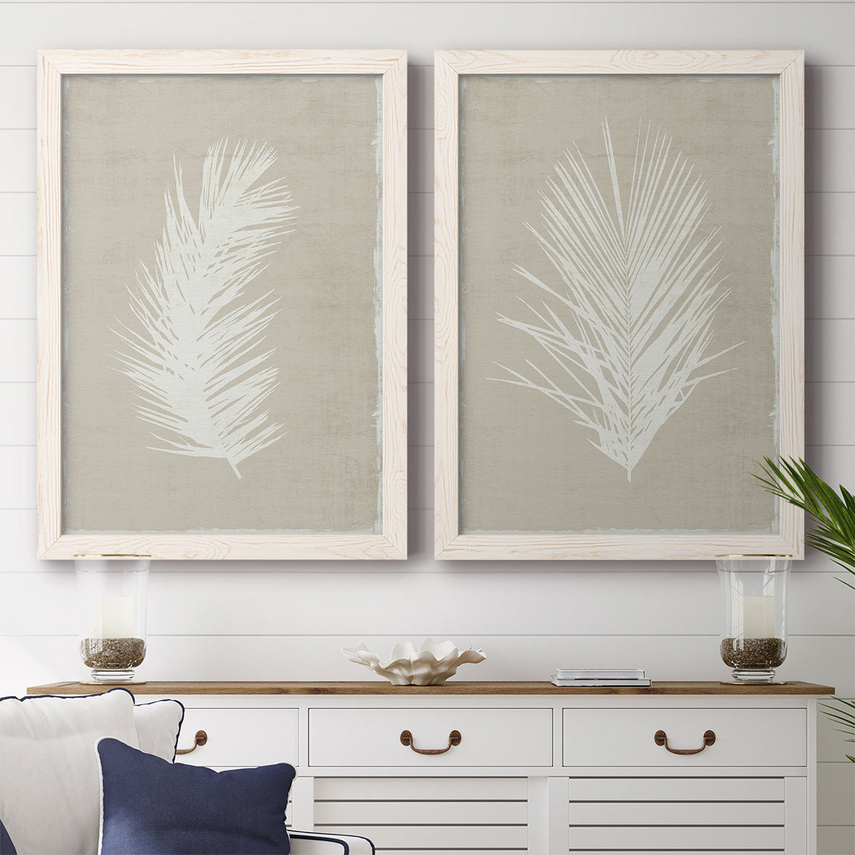 Set of two white barnwood framed canvas prints depicting a coordinated art pair of white palm frond silhouettes rendered as minimalist tropical botanical prints above a dining room sideboard.