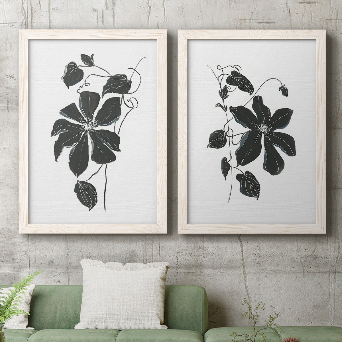 Set of two white barnwood framed canvas prints depicting a coordinated art pair of black leafy vine silhouettes rendered as minimalist botanical prints above a sofa in a modern living room.