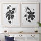 Set of two white barnwood framed canvas prints depicting a coordinated art pair of black leafy vine silhouettes rendered as minimalist botanical prints above a dining room sideboard.