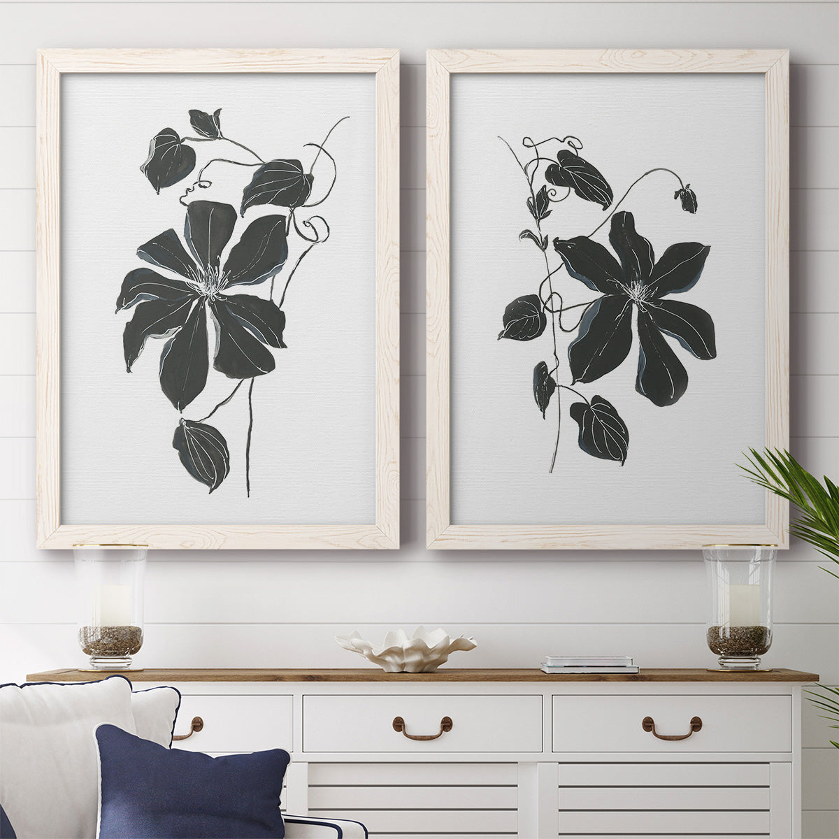 Set of two white barnwood framed canvas prints depicting a coordinated art pair of black leafy vine silhouettes rendered as minimalist botanical prints above a dining room sideboard.