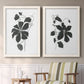 Set of two white barnwood framed canvas prints depicting two minimalist botanical prints featuring black leafy vine silhouettes above a sideboard in a cozy sitting room.