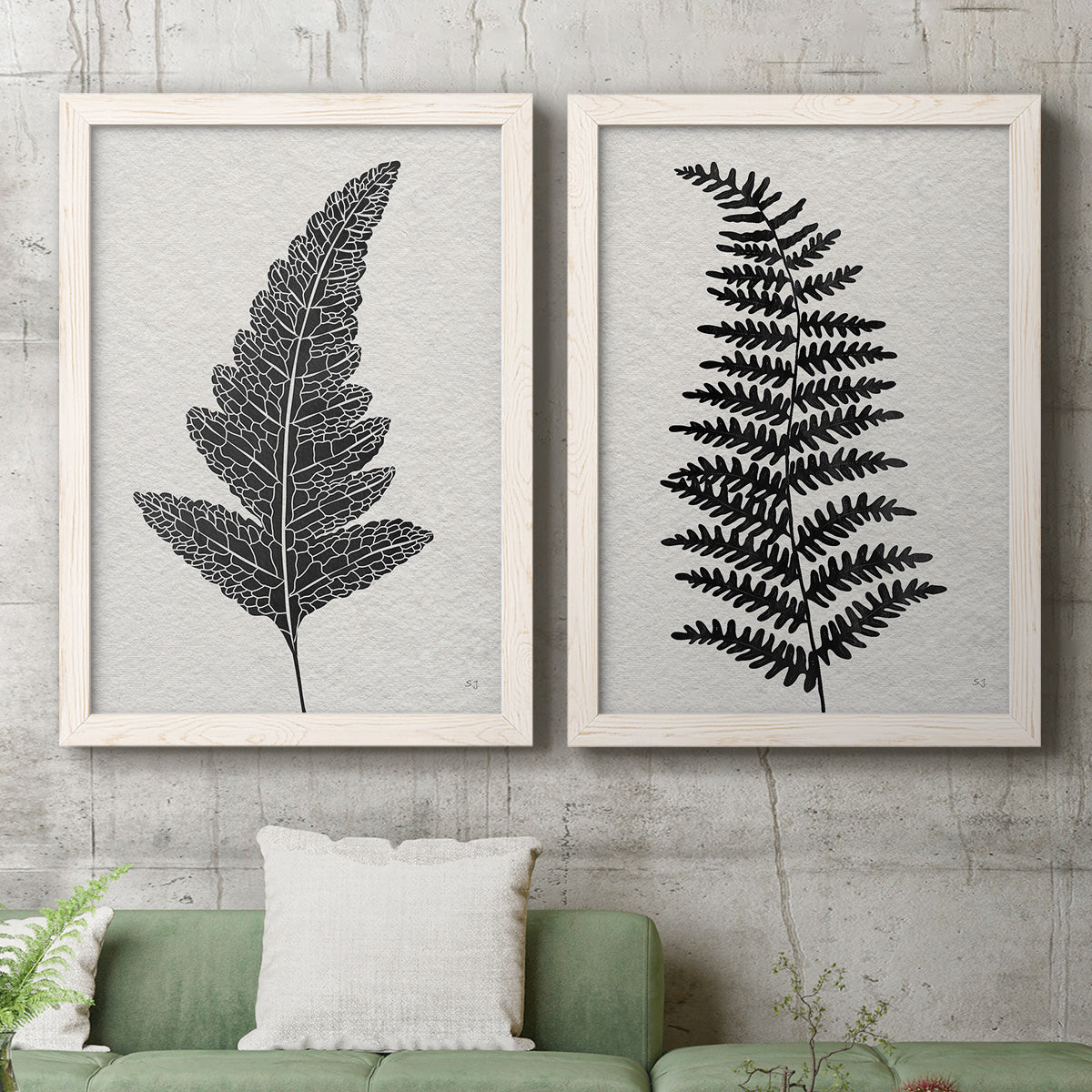 Set of two white barnwood framed canvas prints depicting a coordinated art pair of black fern leaf silhouettes rendered as minimalist botanical prints above a sofa in a modern living room.