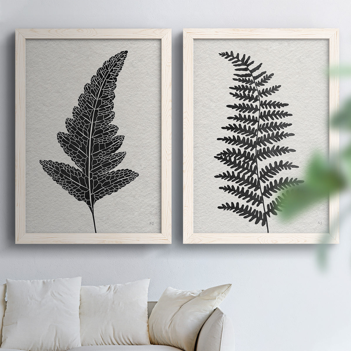 Set of two white barnwood framed canvas prints depicting detailed fronds, high-contrast shapes, and lightly textured cream grounds arranged across two complementary compositions above a sofa in a bright living space.