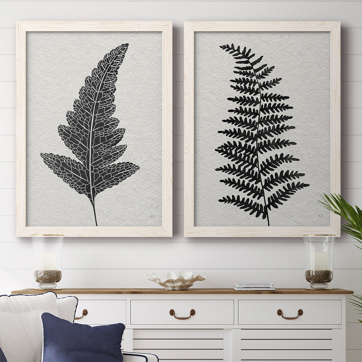 Set of two white barnwood framed canvas prints depicting a coordinated art pair of black fern leaf silhouettes rendered as minimalist botanical prints above a dining room sideboard.