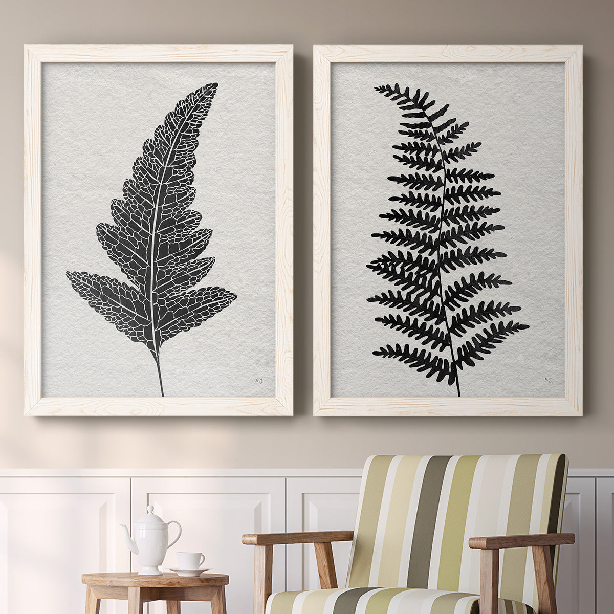 Set of two white barnwood framed canvas prints depicting two minimalist botanical prints featuring black fern leaf silhouettes above a sideboard in a cozy sitting room.