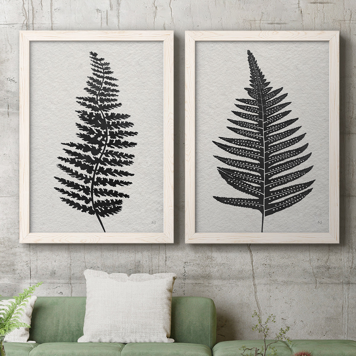 Set of two white barnwood framed canvas prints depicting a coordinated art pair of black fern leaf silhouettes rendered as minimalist botanical prints above a sofa in a modern living room.