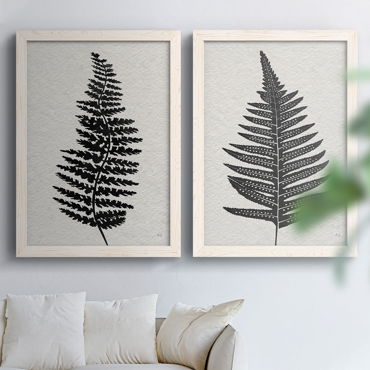 Set of two white barnwood framed canvas prints depicting detailed fronds, high-contrast shapes, and lightly textured cream grounds arranged across two complementary compositions above a sofa in a bright living space.