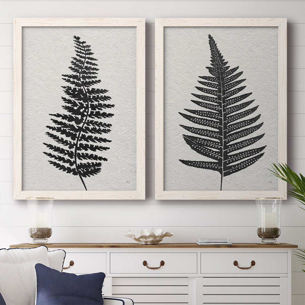 Set of two white barnwood framed canvas prints depicting a coordinated art pair of black fern leaf silhouettes rendered as minimalist botanical prints above a dining room sideboard.