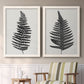 Set of two white barnwood framed canvas prints depicting two minimalist botanical prints featuring black fern leaf silhouettes above a sideboard in a cozy sitting room.