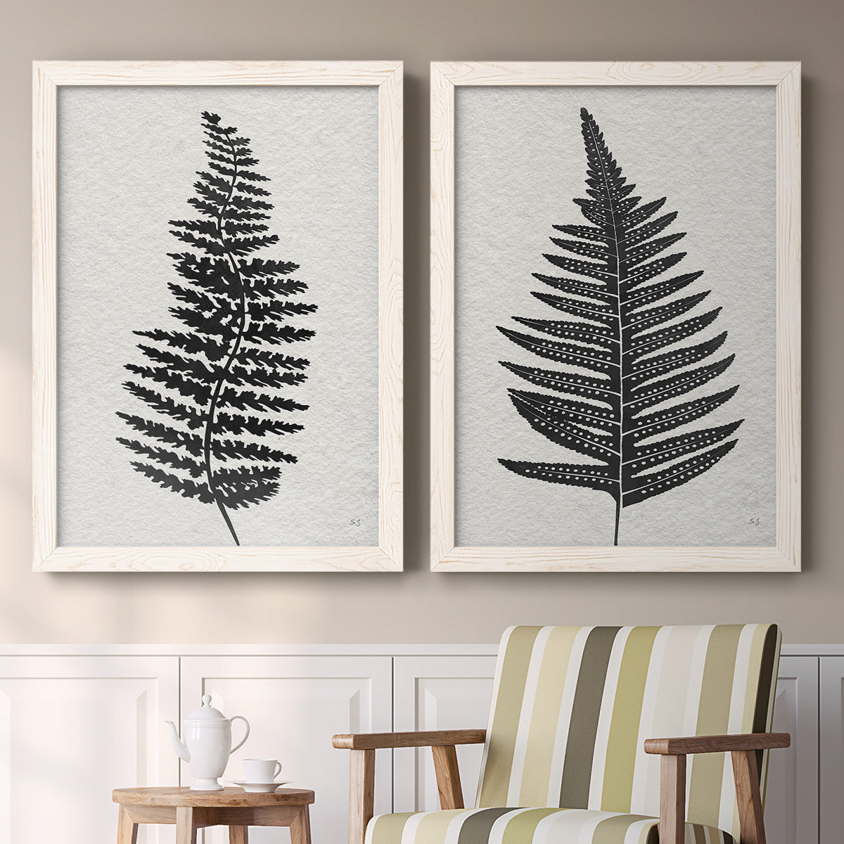 Set of two white barnwood framed canvas prints depicting two minimalist botanical prints featuring black fern leaf silhouettes above a sideboard in a cozy sitting room.