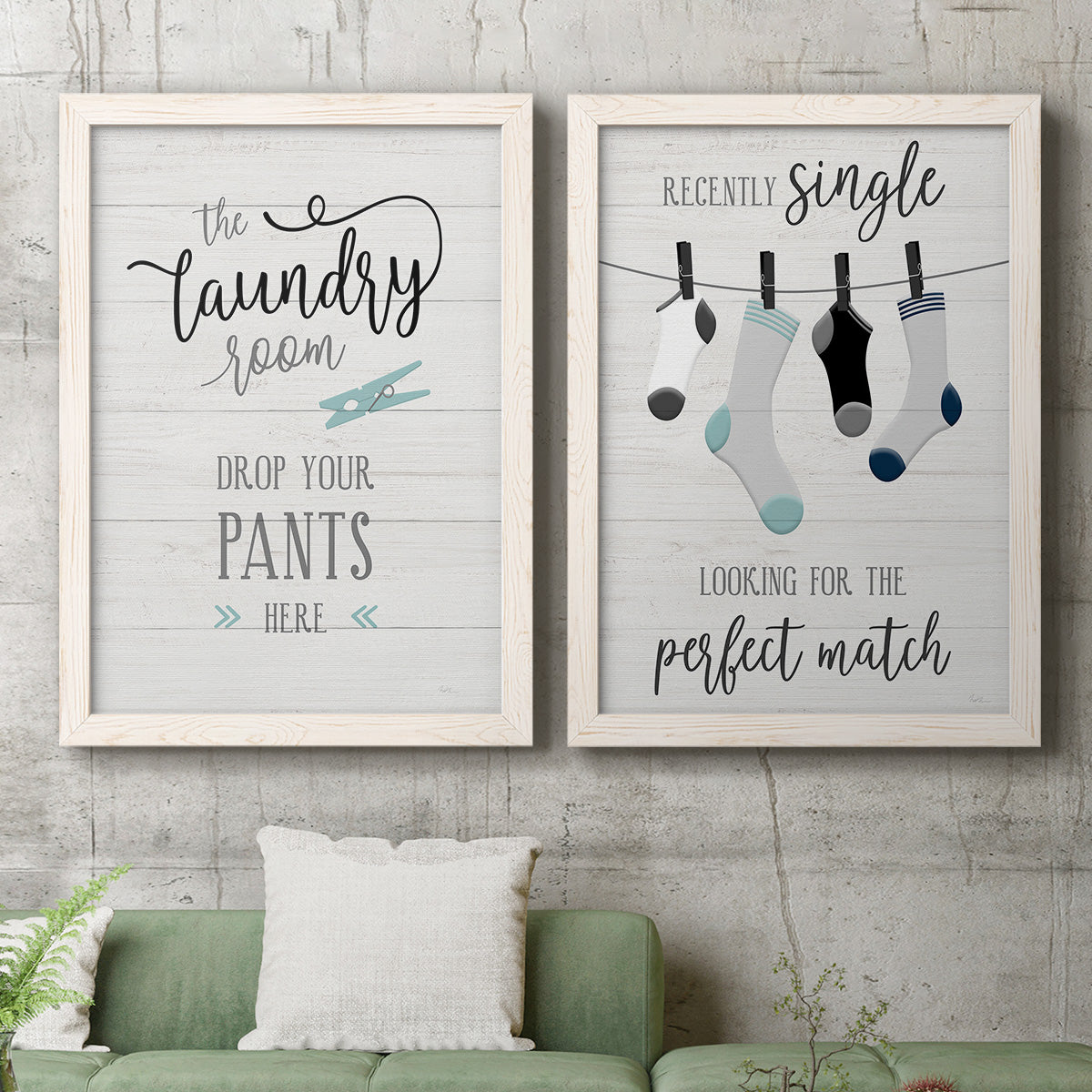 Set of two white barnwood framed canvas prints depicting a coordinated art pair of humorous laundry-room sayings and clothing icons rendered as rustic typographic wall art above a sofa in a modern living room.
