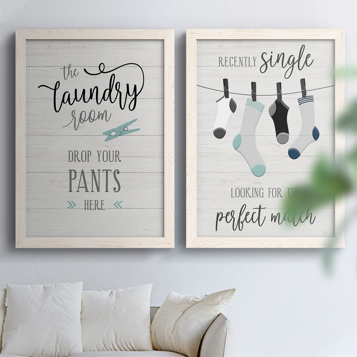 Set of two white barnwood framed canvas prints depicting hand-lettered phrases, socks hangers and laundry symbols on linen texture arranged across two complementary compositions above a sofa in a bright living space.
