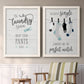 Set of two white barnwood framed canvas prints depicting two rustic typographic wall art featuring humorous laundry-room sayings and clothing icons above a sideboard in a cozy sitting room.
