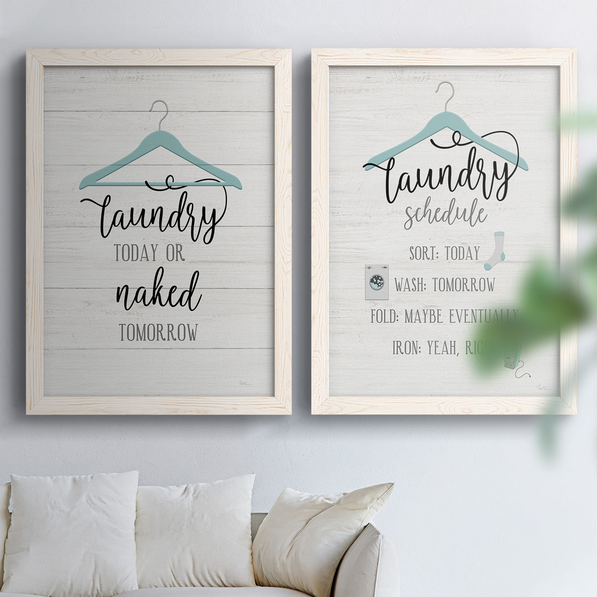Set of two white barnwood framed canvas prints depicting hand-lettered phrases, socks hangers and laundry symbols on linen texture arranged across two complementary compositions above a sofa in a bright living space.