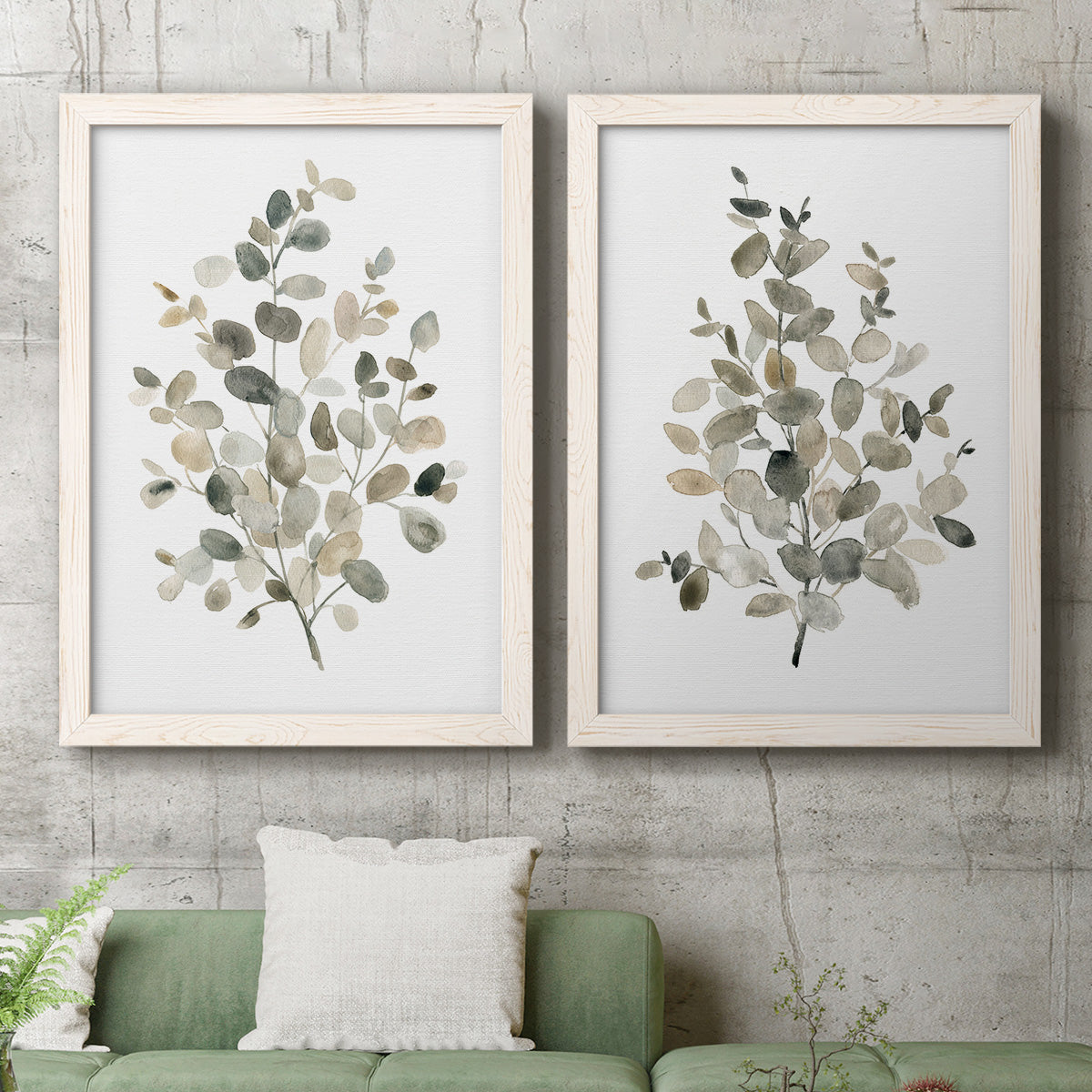 Set of two white barnwood framed canvas prints depicting a coordinated art pair of delicate eucalyptus branches with rounded leaves rendered as minimalist watercolor botanical studies above a sofa in a modern living room.