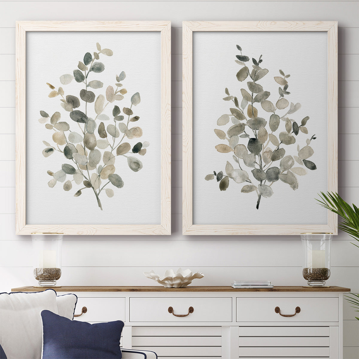 Set of two white barnwood framed canvas prints depicting a coordinated art pair of delicate eucalyptus branches with rounded leaves rendered as minimalist watercolor botanical studies above a dining room sideboard.