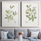 Set of two white barnwood framed canvas prints depicting paired farmhouse herb illustrations with simple green leaves, fine stems, and clean cream grounds above a sofa in a contemporary living room.