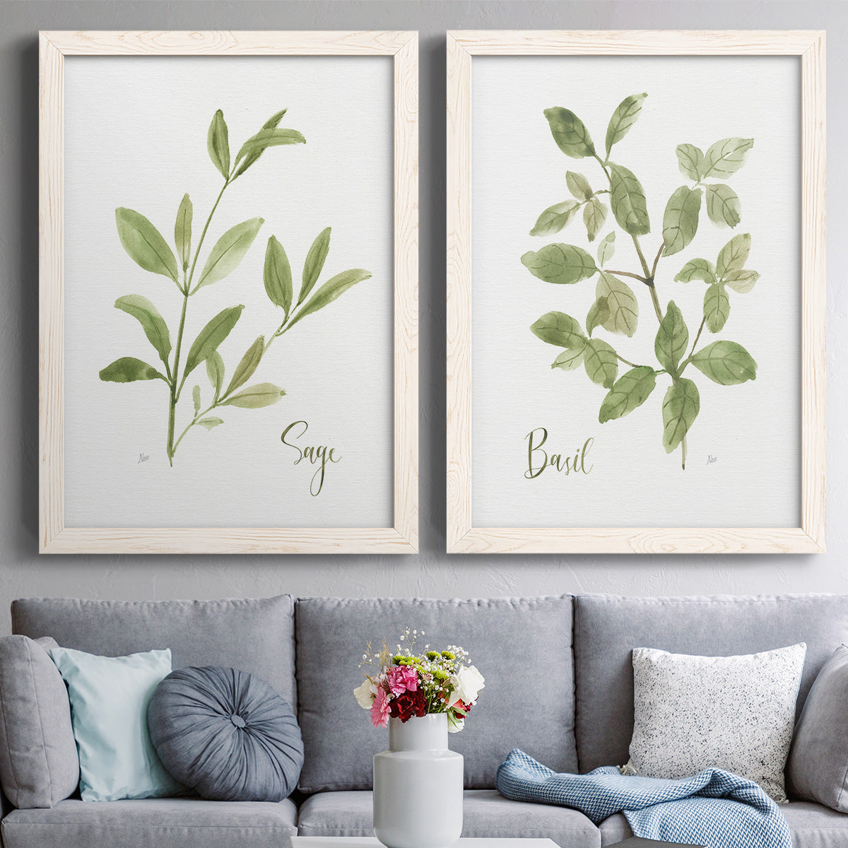 Set of two white barnwood framed canvas prints depicting paired farmhouse herb illustrations with simple green leaves, fine stems, and clean cream grounds above a sofa in a contemporary living room.