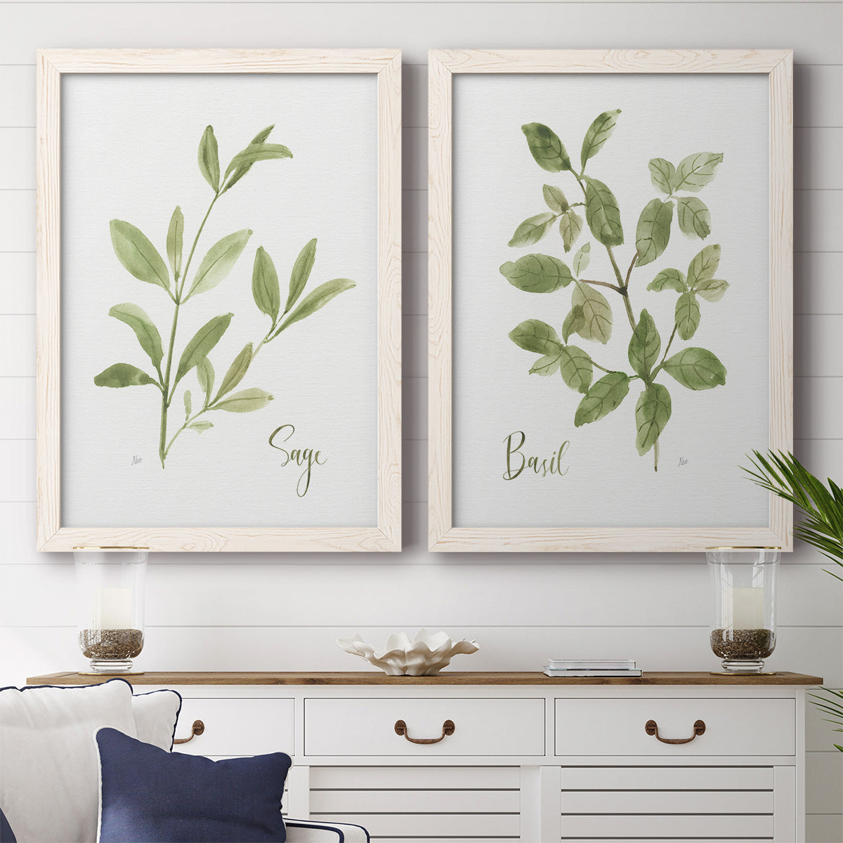 Set of two white barnwood framed canvas prints depicting a coordinated art pair of culinary sage and basil sprigs with handwritten labels rendered as farmhouse herb illustrations above a dining room sideboard.