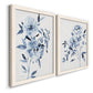Angled view of a set of two white barnwood framed canvas prints featuring two expressive watercolor botanical paintings featuring loose blue flowers and leafy branches.