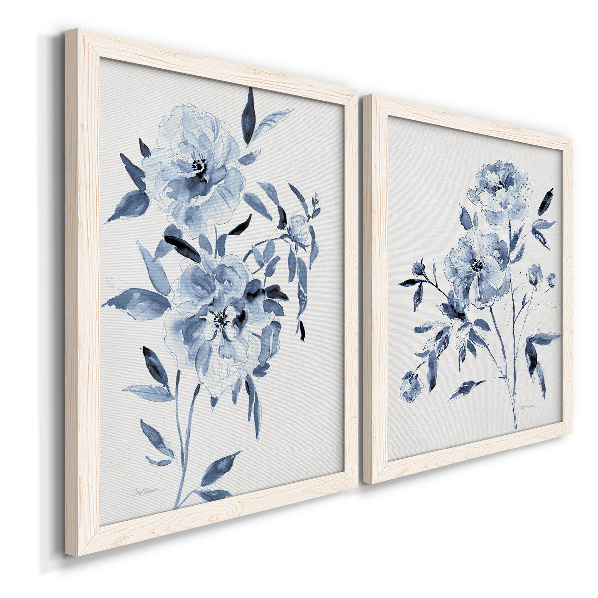 Angled view of a set of two white barnwood framed canvas prints featuring two expressive watercolor botanical paintings featuring loose blue flowers and leafy branches.