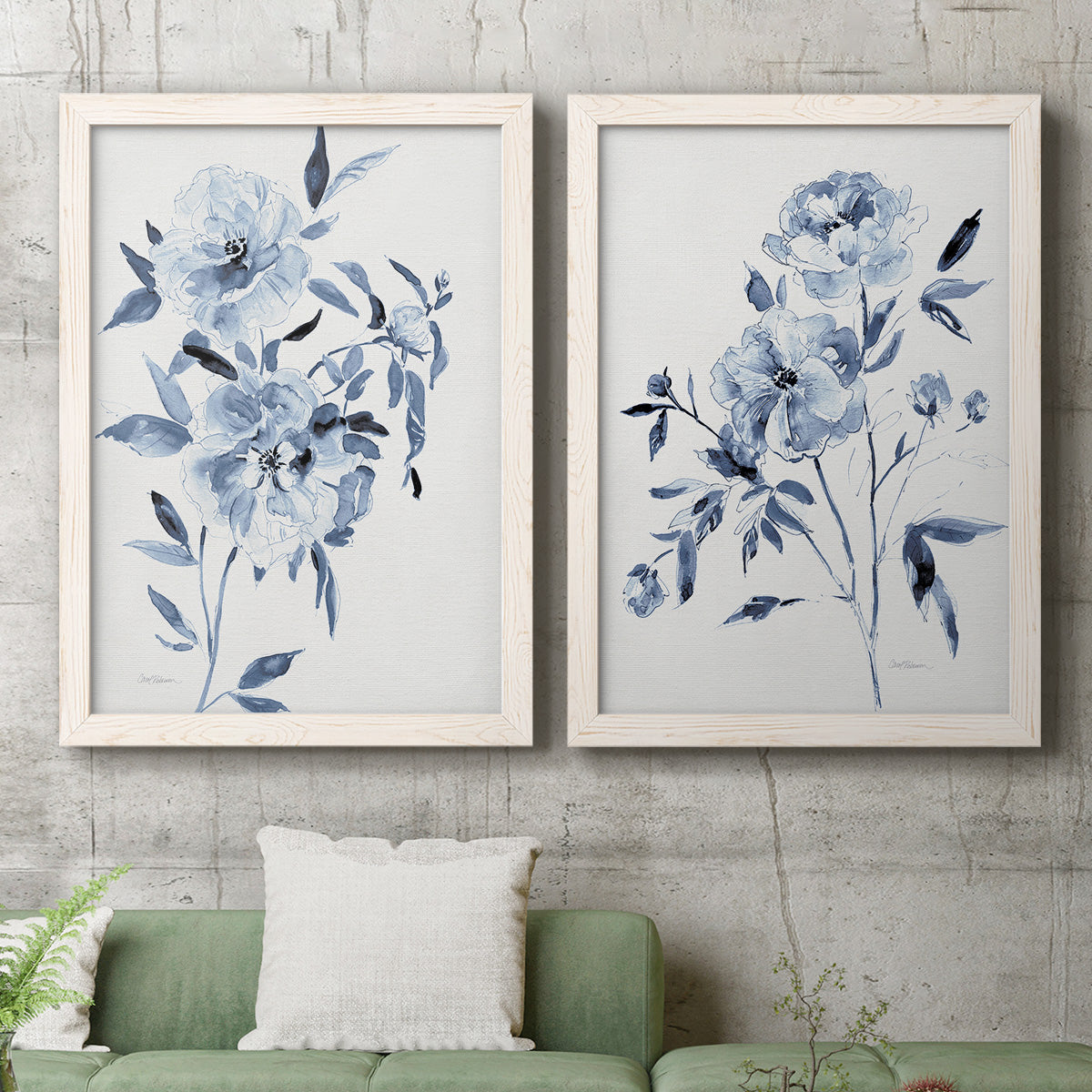 Set of two white barnwood framed canvas prints depicting a coordinated art pair of loose blue flowers and leafy branches rendered as expressive watercolor botanical paintings above a sofa in a modern living room.