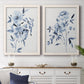 Set of two white barnwood framed canvas prints depicting a coordinated art pair of loose blue flowers and leafy branches rendered as expressive watercolor botanical paintings above a dining room sideboard.
