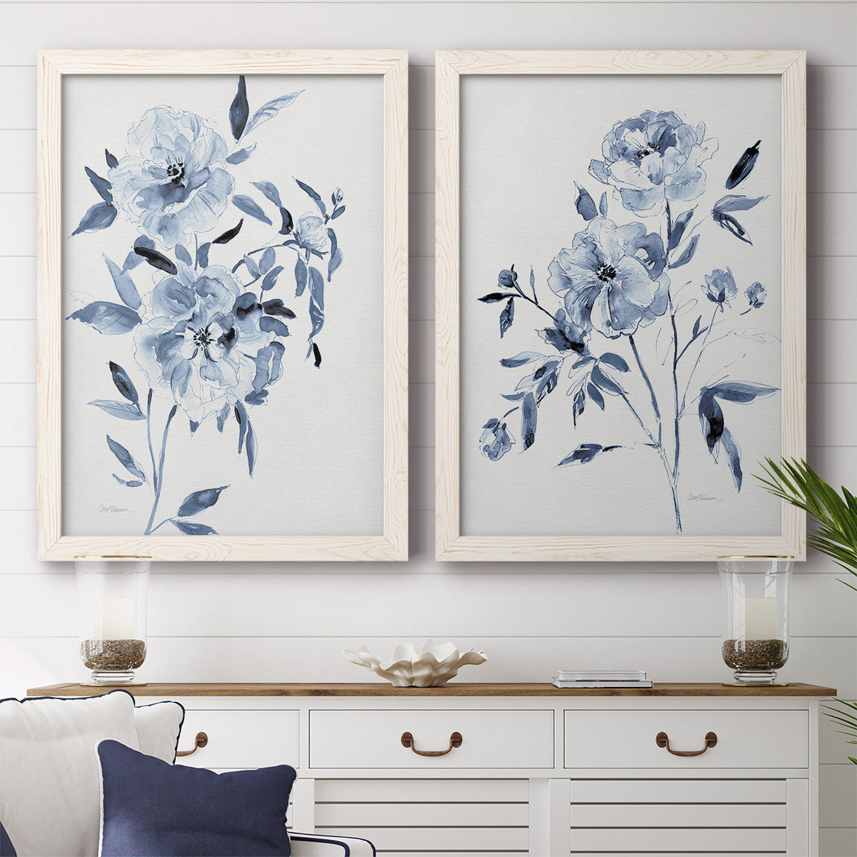 Set of two white barnwood framed canvas prints depicting a coordinated art pair of loose blue flowers and leafy branches rendered as expressive watercolor botanical paintings above a dining room sideboard.