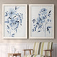Set of two white barnwood framed canvas prints depicting two expressive watercolor botanical paintings featuring loose blue flowers and leafy branches above a sideboard in a cozy sitting room.