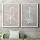 Set of two white barnwood framed canvas prints depicting a coordinated art pair of white botanical silhouettes on softly weathered neutral backgrounds rendered as rustic minimalist botanical prints above a sofa in a modern living room.