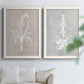 Set of two white barnwood framed canvas prints depicting delicate stems, leaves, and blossoms against gray taupe and pale blue panels arranged across two complementary compositions above a sofa in a bright living space.