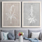 Set of two white barnwood framed canvas prints depicting paired rustic minimalist botanical prints with delicate stems, leaves, and blossoms against gray taupe and pale blue panels above a sofa in a contemporary living room.