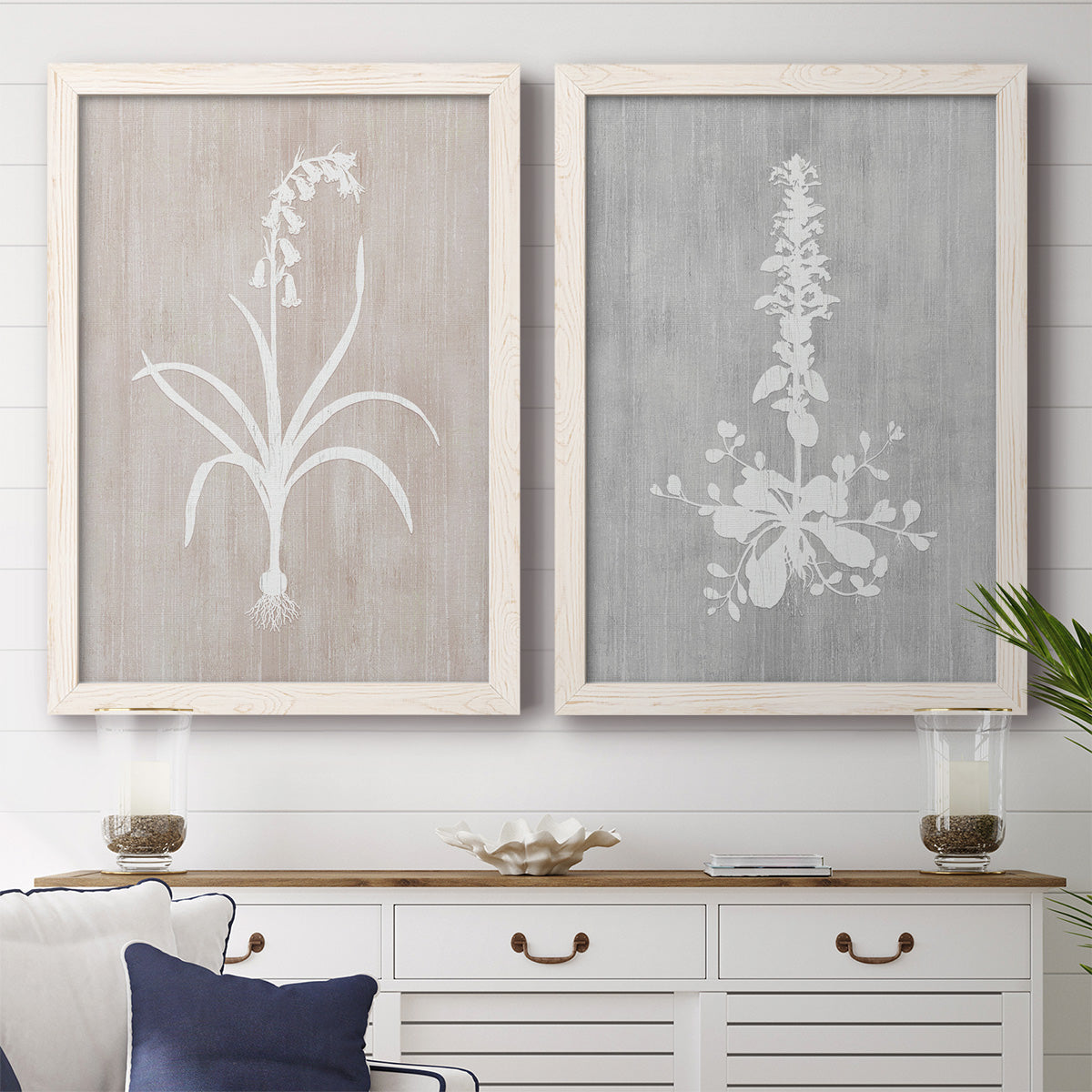 Set of two white barnwood framed canvas prints depicting a coordinated art pair of white botanical silhouettes on softly weathered neutral backgrounds rendered as rustic minimalist botanical prints above a dining room sideboard.