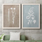 Set of two white barnwood framed canvas prints depicting a coordinated art pair of white botanical silhouettes on softly weathered neutral backgrounds rendered as rustic minimalist botanical prints above a sofa in a modern living room.
