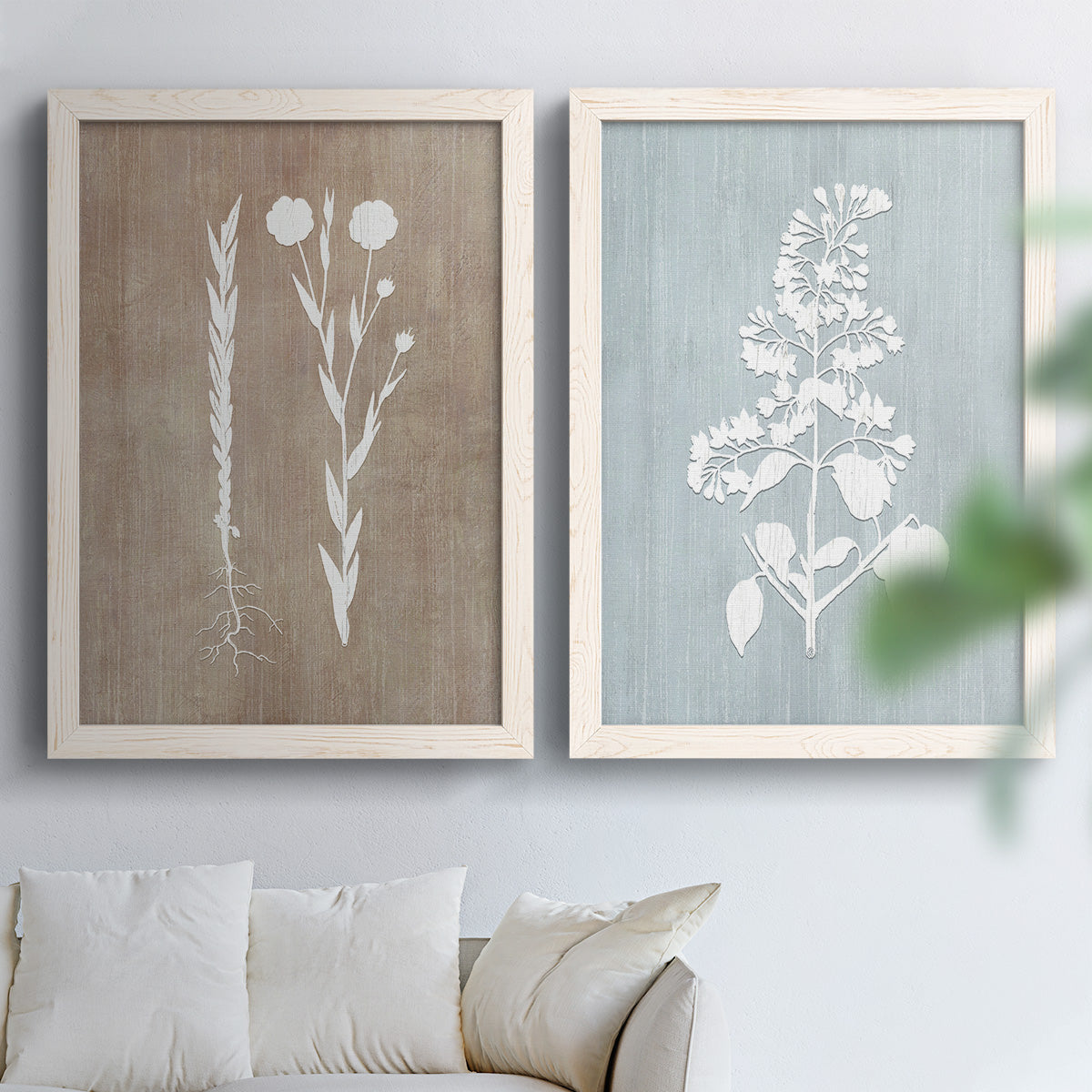 Set of two white barnwood framed canvas prints depicting delicate stems, leaves, and blossoms against gray taupe and pale blue panels arranged across two complementary compositions above a sofa in a bright living space.