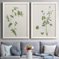 Set of two white barnwood framed canvas prints depicting paired rustic minimalist botanical studies with fine green branches, sparse blue or white blossoms, and cream grounds above a sofa in a contemporary living room.
