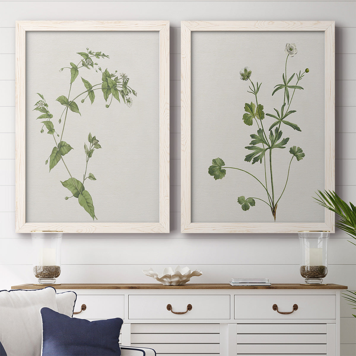 Set of two white barnwood framed canvas prints depicting a coordinated art pair of delicate wildflower and leafy stems rendered as rustic minimalist botanical studies above a dining room sideboard.
