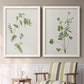 Set of two white barnwood framed canvas prints depicting two rustic minimalist botanical studies featuring delicate wildflower and leafy stems above a sideboard in a cozy sitting room.