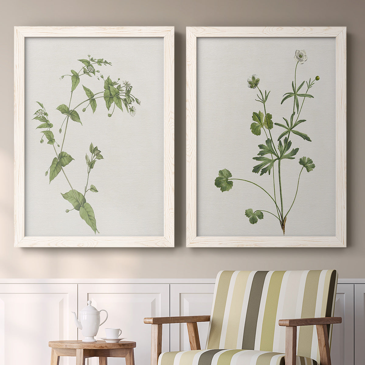 Set of two white barnwood framed canvas prints depicting two rustic minimalist botanical studies featuring delicate wildflower and leafy stems above a sideboard in a cozy sitting room.