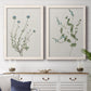 Set of two white barnwood framed canvas prints depicting a coordinated art pair of delicate wildflower and leafy stems rendered as rustic minimalist botanical studies above a dining room sideboard.