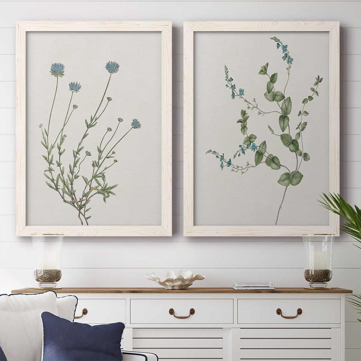 Set of two white barnwood framed canvas prints depicting a coordinated art pair of delicate wildflower and leafy stems rendered as rustic minimalist botanical studies above a dining room sideboard.